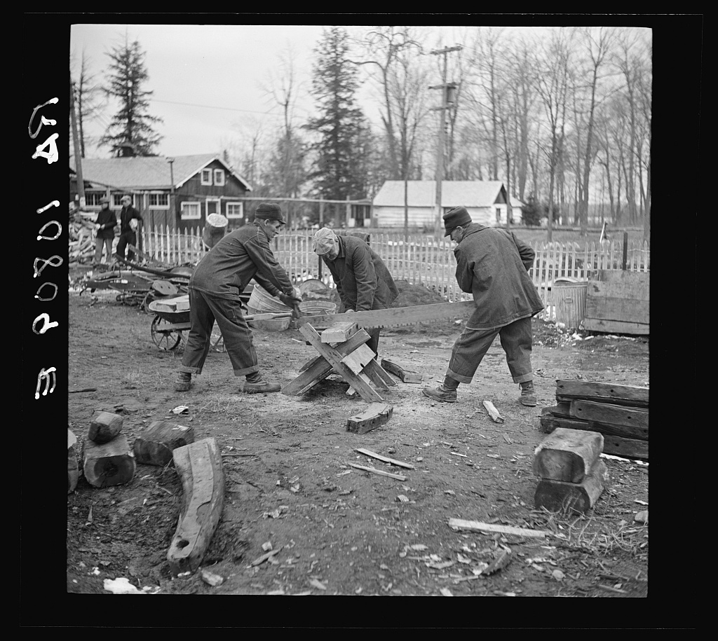 Three men use a saw to cut wood in a yard.