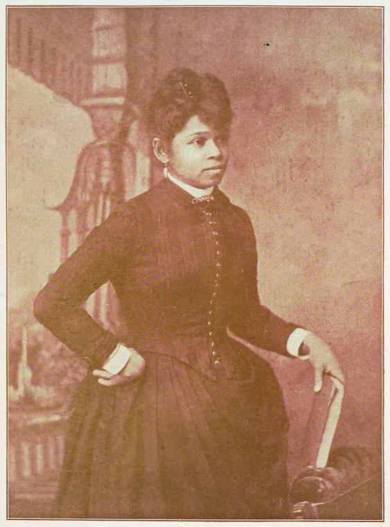 3/4 body photo of Annie L. Burton standing facing right, with her right hand holding a book and her left hand on her hip.