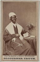Sojourner Truth seated beside a table with a vase of flowers. She is looking at the camera and holding yarn in one hand.