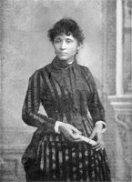 3/4 body photo of Lucy E. Parsons standing. She is holding document in both hands.