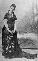 Full body photo of Hallie Quinn Brown standing with her hands held below her waist. She is wearing a floor-length gown with floral details. 