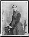 3/4 body photo of Frances E. W. Harper standing with her hands on a chair, looking front.