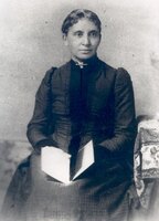 3/4 body photo of Charlotte Forten Grimké seated and holding a book, looking right. 