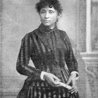 3/4 body photo of Lucy E. Parsons standing. She is holding document in both hands.