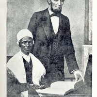 Sojourner Truth seated at a table with an open book on it. Abraham Lincoln stands next to Sojourner Truth and is looking at the book. 