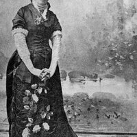 Full body photo of Hallie Quinn Brown standing with her hands held below her waist. She is wearing a floor-length gown with floral details. 