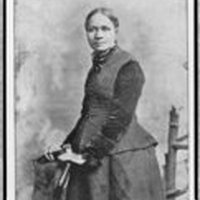 3/4 body photo of Frances E. W. Harper standing with her hands on a chair, looking front.