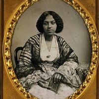 3/4 body photo of a seated African American woman. She is wearing elaborate attire and holding a book. The portrait is in a gold frame.