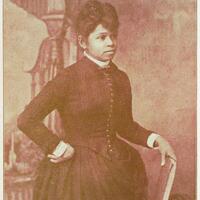 3/4 body photo of Annie L. Burton standing facing right, with her right hand holding a book and her left hand on her hip.