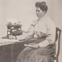3/4 body photo of L. A. J. Moorer seated, holding a pen in one hand and a book in the other.