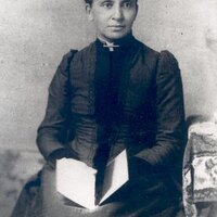 3/4 body photo of Charlotte Forten Grimké seated and holding a book, looking right. 