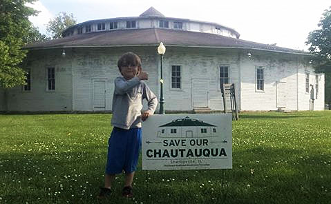 Photograph of a child standing next to a "Save Our Chautauqua" sign on Shelbyville Chautauqua Auditorium grounds.