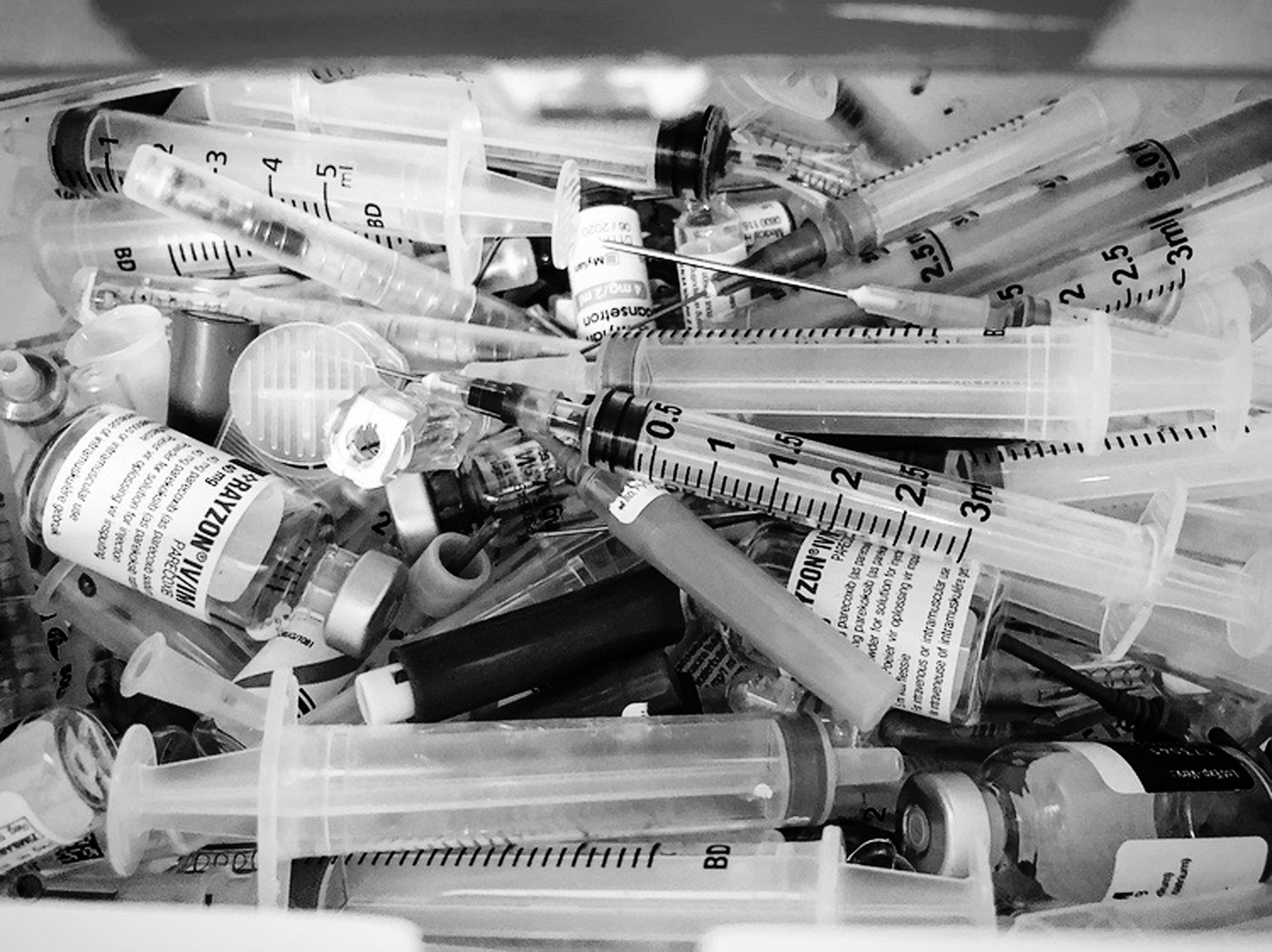 Black and white picture of syringes and viles of medicines drawn up by syringe