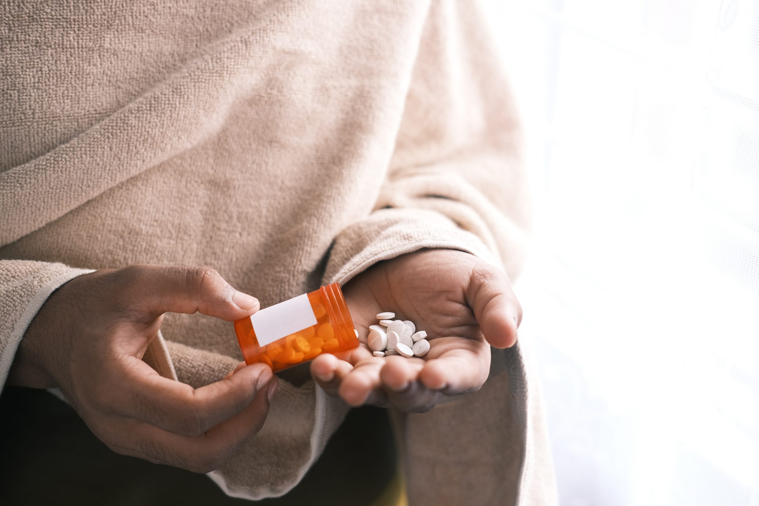 Picture of a person pouring white pills from a prescription bottle into their hand