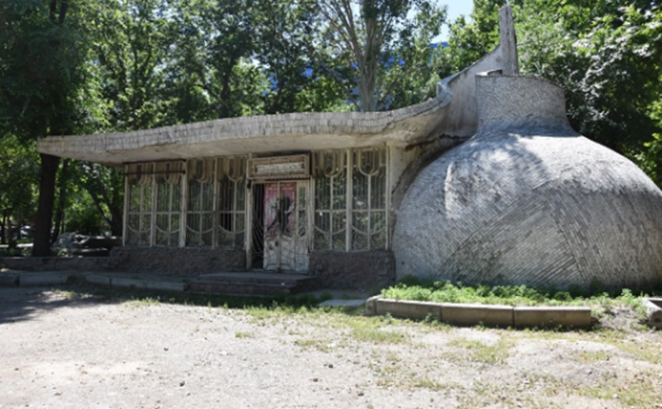 The now closed Café Ulitka in Bishkek, protected by bars and surrounded by tall green trees.