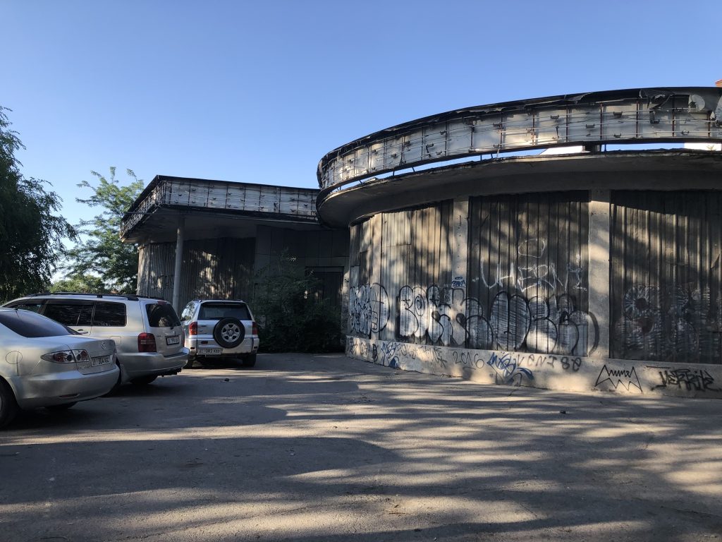 The Bishkek Planetarium with several cars parked in front of the building.