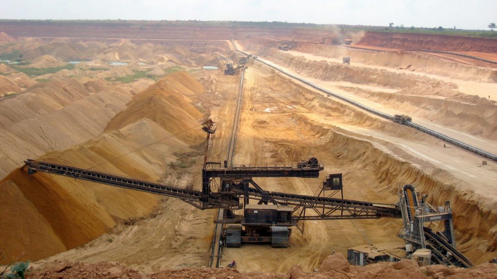A large piece of machinery is situated in a brown mining quarry.