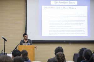 Nelson lecturing. Background: screen showing New York times article "DNA Offers Link to Black History"