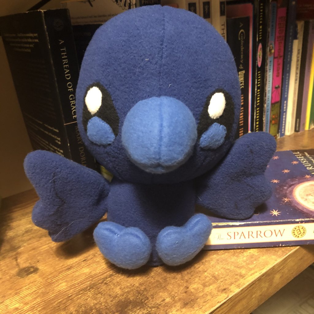 Blue bird plush sitting on a bookshelf.